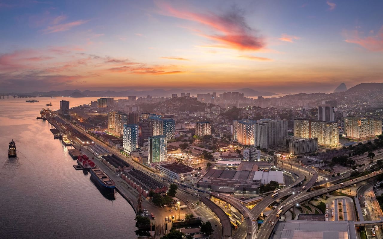 Vista aérea da zona portuária do Rio ao entardecer, com o cais, a Baía de Guanabara e o Pão de Açúcar ao fundo